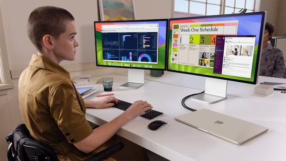A person sitting at a desk with two computers

Description automatically generated